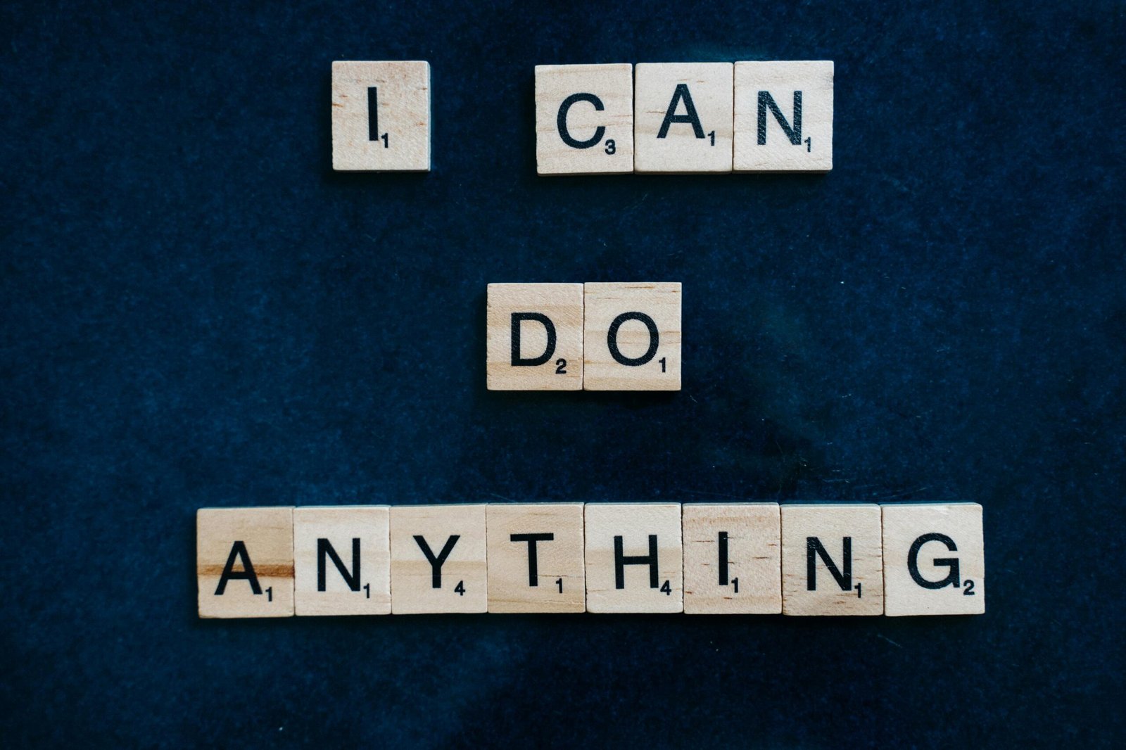 Inspirational phrase 'I Can Do Anything' created with Scrabble tiles on a blue surface.